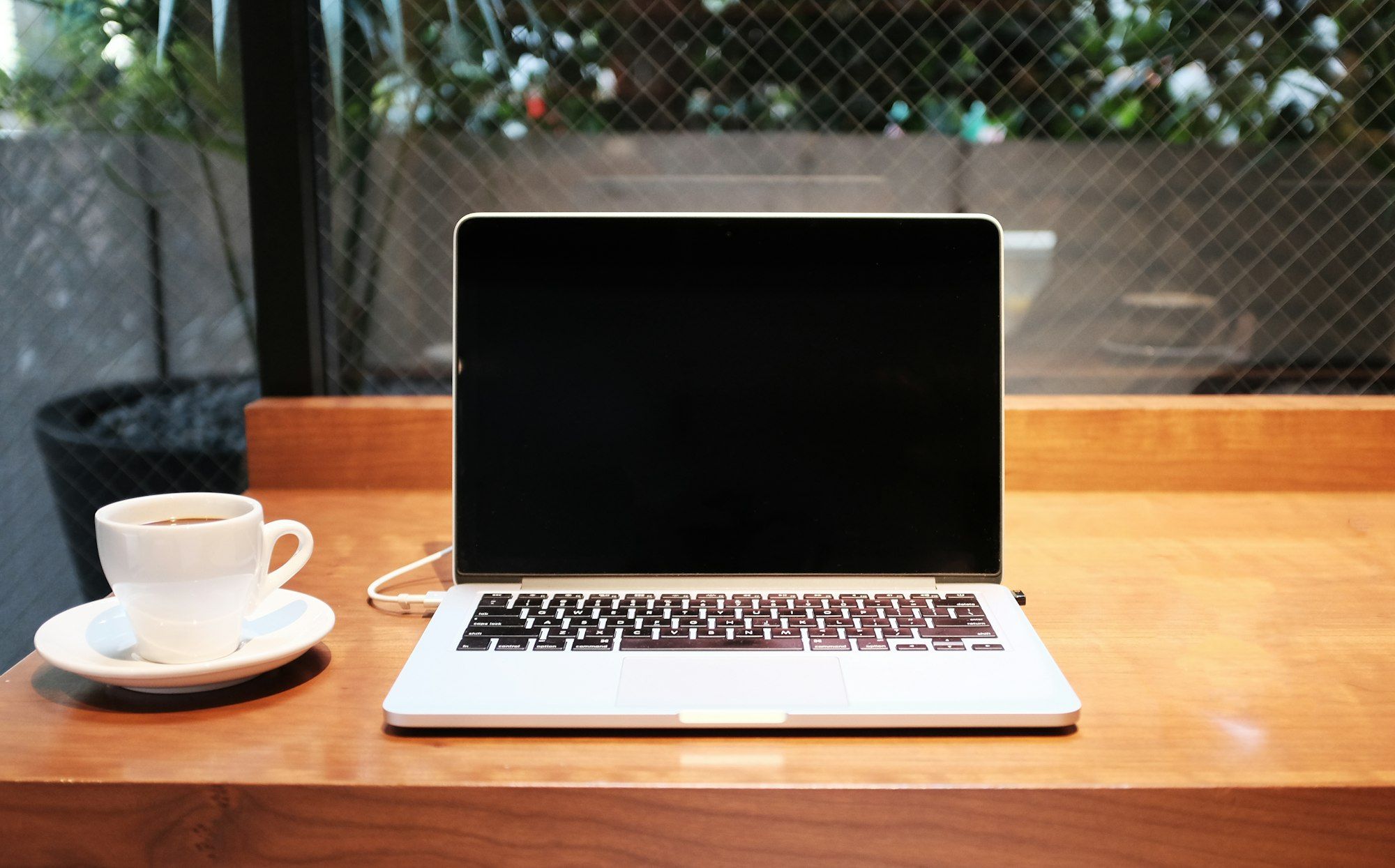 A laptop on a wooden desk beside a cup of coffee