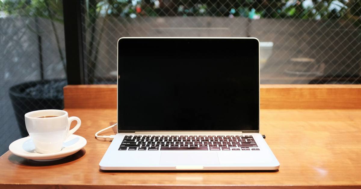 A laptop on a wooden desk beside a cup of coffee