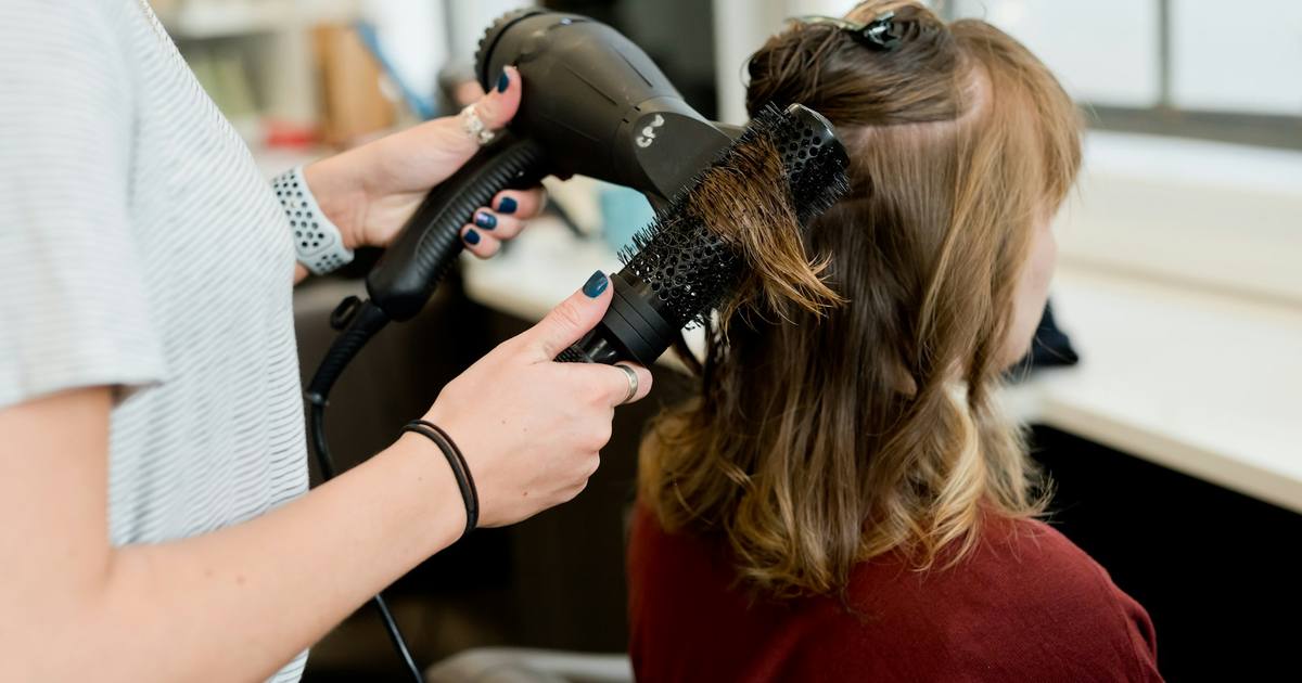 A hairstylist blow-drying a client's hair in a salon