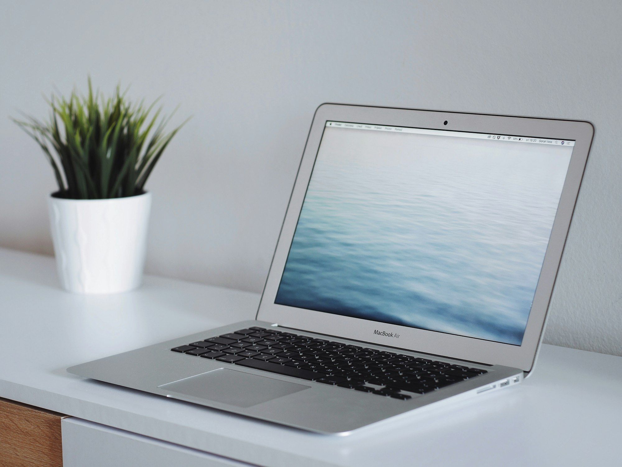 A laptop beside a small potted plant on a white desk