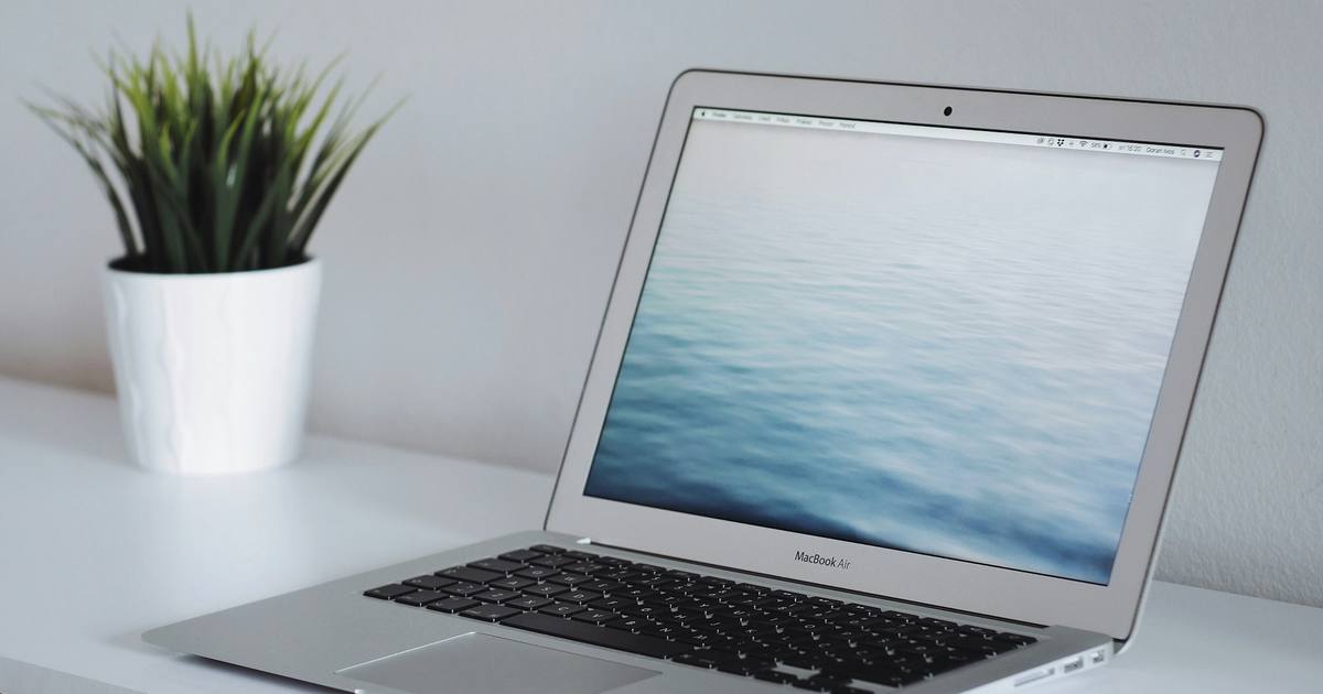 A laptop beside a small potted plant on a white desk