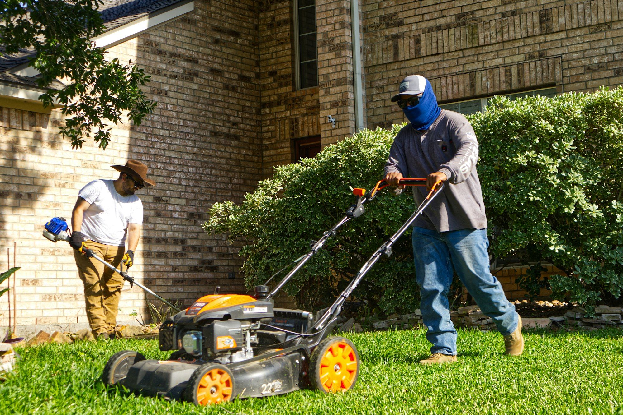 Two lawn care workers mowing and trimming a front yard