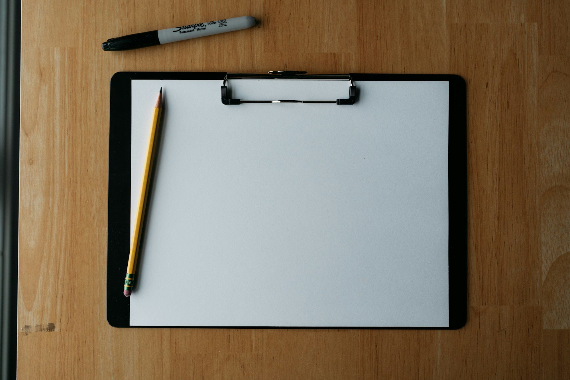 A blank clipboard with a pencil and pen on a wooden table
