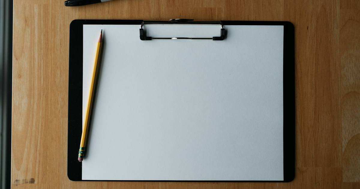 A blank clipboard with a pencil and pen on a wooden table