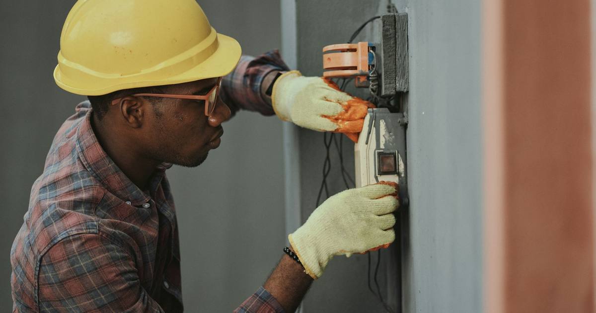 An electrician in a yellow hard hat working on wiring